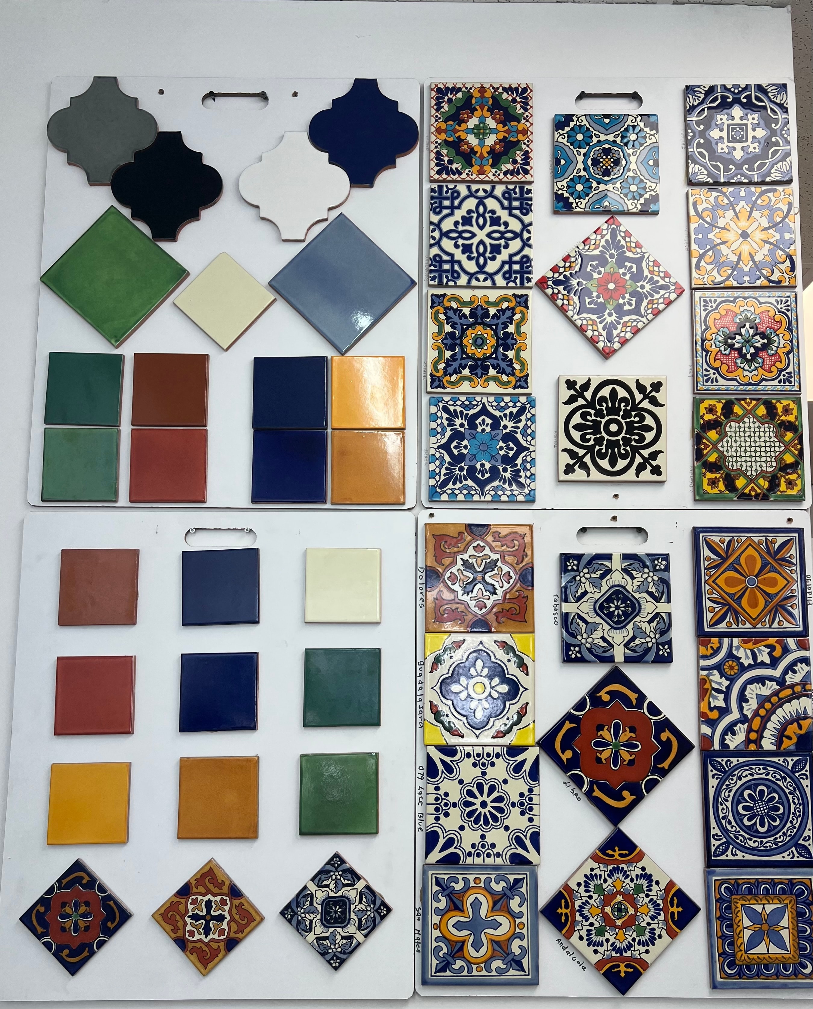 Mexican decorative tile sample boards showing hand-painted patterns, solid colors, and arabesque shapes in navy, green, rust, gold, and cream